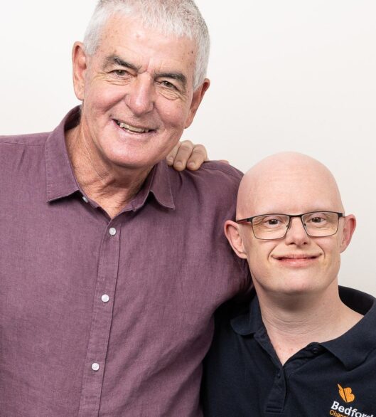 Ryan stands beside his dad, Doug, in a studio portrait against a light grey background.